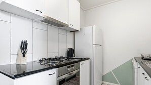 Una cucina compatta con mobili bianchi, fornelli a gas, forno integrato e frigorifero.