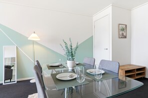 A modern dining area with a glass table, chairs, a potted plant, and a lamp. - Stunning CBD Penthouse Top-Floor Living with Pool, Gym & Skyline Views (Melbourne)