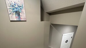 Una esquina de una habitación con suelo de madera, una puerta blanca y una obra de arte colgada en la pared.