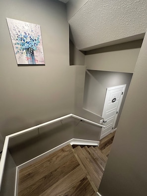A corner of a room with a wooden floor, a white door, and a wall-mounted artwork. - Spacious 2-bedroom Basement Suite Near West Edmonton Mall. (Edmonton)