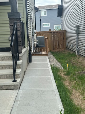 A residential area with a concrete pathway leading to a wooden deck, surrounded by houses with siding and a stone accent wall. - Spacious 2-bedroom Basement Suite Near West Edmonton Mall. (Edmonton)