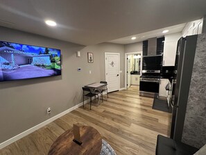 A modern living room with a flat-screen TV, a dining table, and a kitchen area with a stove and cabinets. - Spacious 2-bedroom Basement Suite Near West Edmonton Mall. (Edmonton)