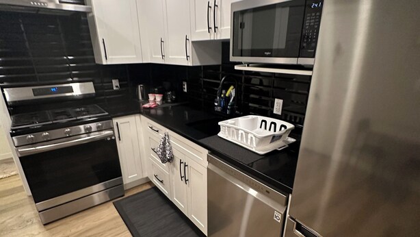 Una cocina moderna con electrodomésticos de acero inoxidable, armarios blancos y encimera negra.