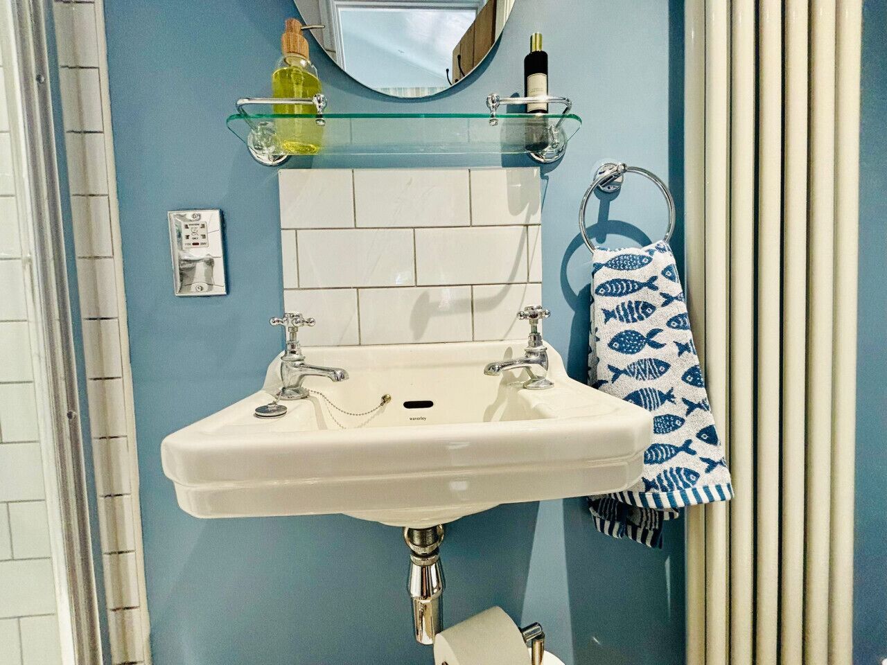 Een badkamer met een wit wastafel, een glazen plank erboven en een handdoekhouder met een handdoek.