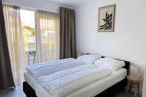 Ein Schlafzimmer mit Bett, Vorhängen, einem Fenster und einem an der Wand hängenden Bild.
