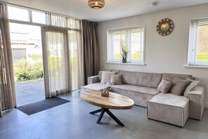 A modern living room with a sectional sofa, a round coffee table, and a large window with blinds.