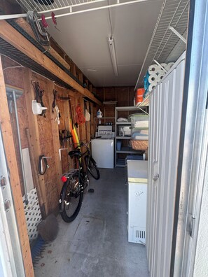 A narrow storage room with wooden walls, a bicycle, a washing machine, and shelves with various items. - Cozy Florida Retreat w/Spacious Porch (Zephyrhills)