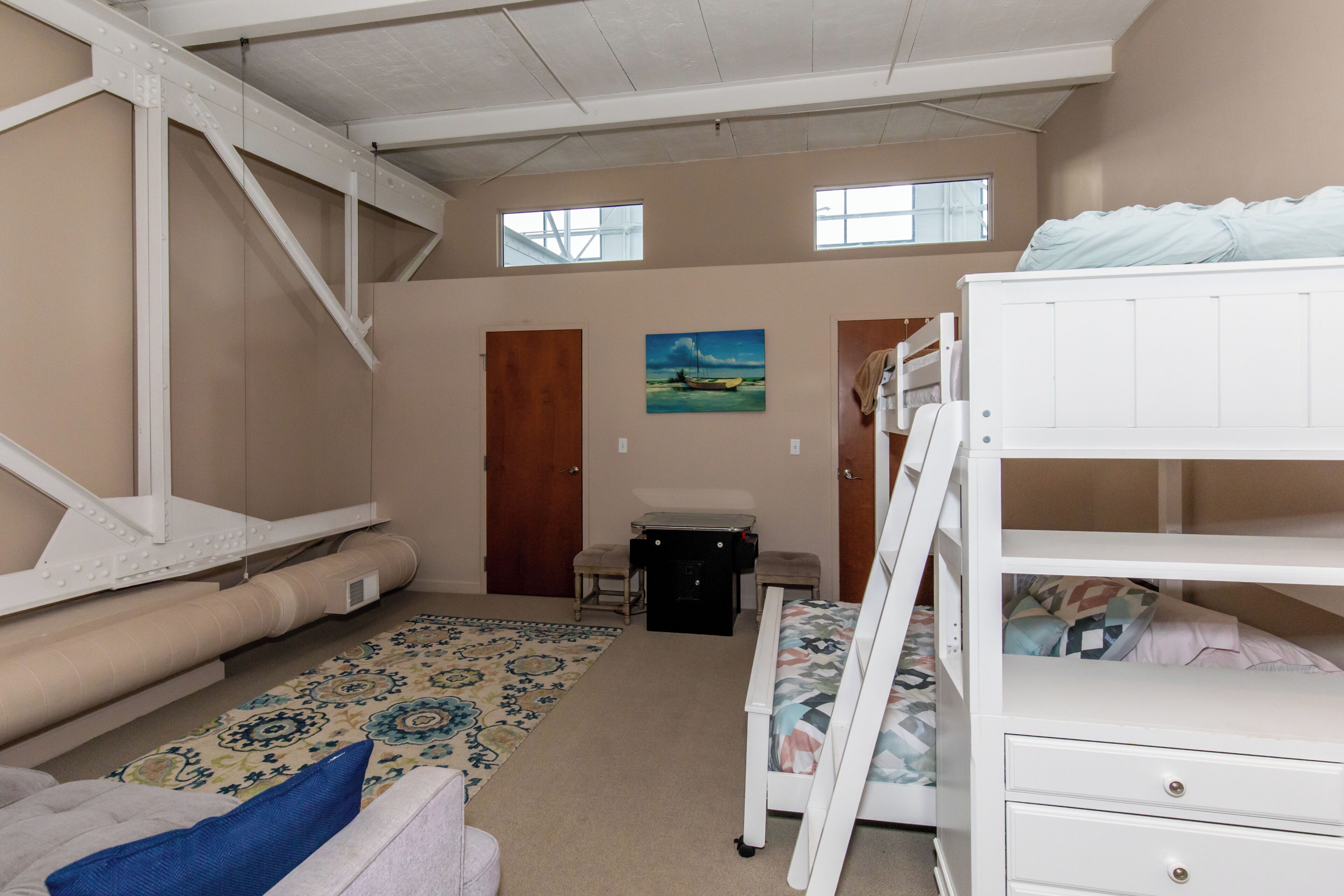 A room with bunk beds, a desk, a chair, a small table, a rug, and a painting on the wall.