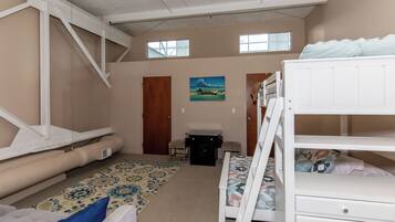 A room with bunk beds, a desk, a chair, a small table, a rug, and a painting on the wall.