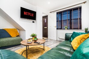 A living room with a sofa, a coffee table with snacks, a TV displaying 'NETFLIX,' and a window with blinds. - 30% OFF| Secures| Parking |Garden| Netflix|2BR|Sleeps5 (Nottingham)