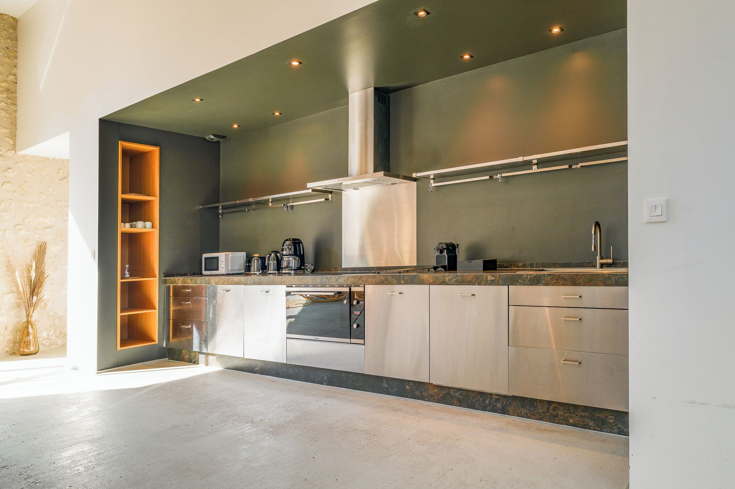Una cocina moderna con electrodomésticos integrados, una campana extractora de acero inoxidable y un estante de madera.