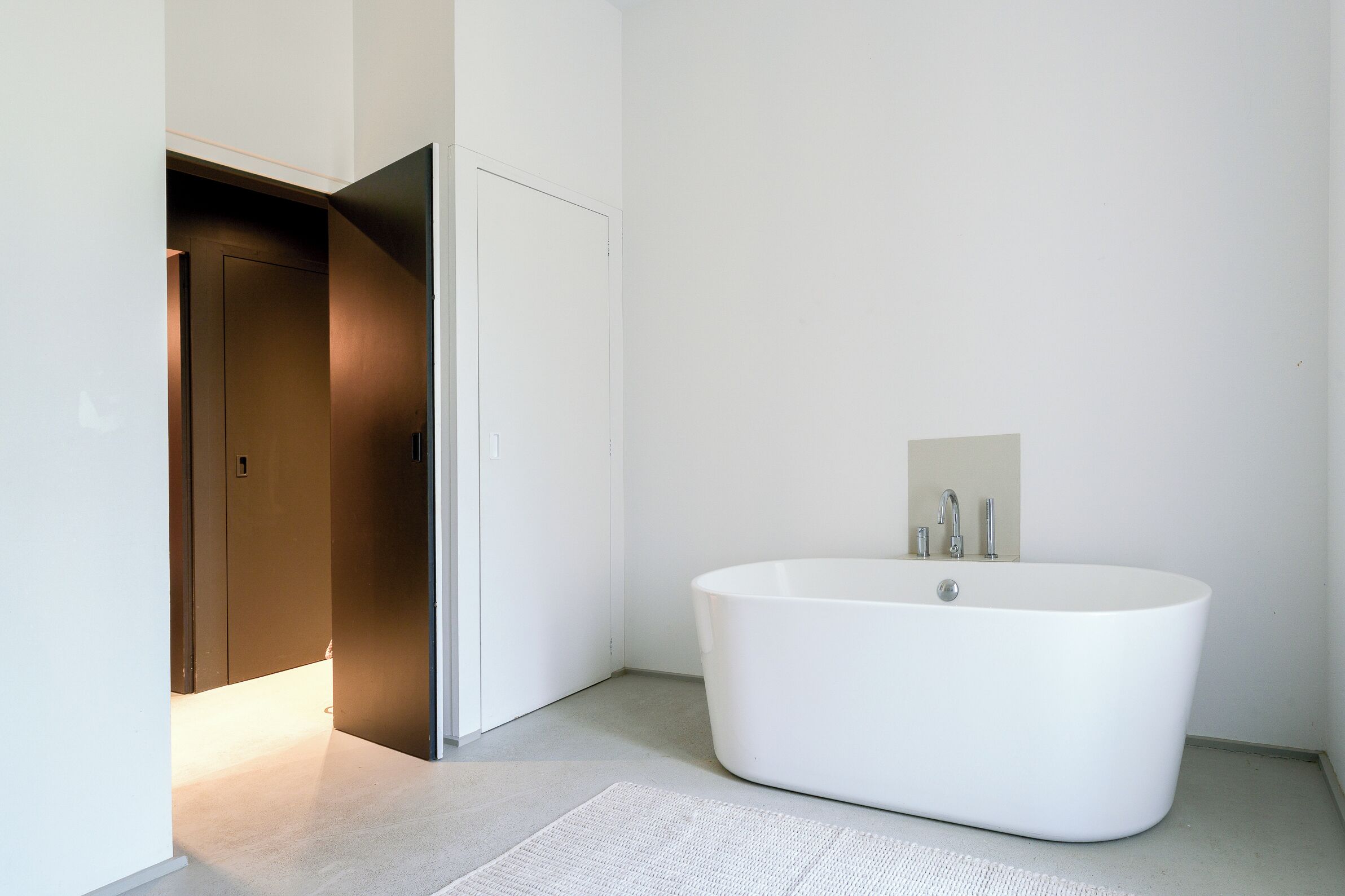 A modern bathroom with a freestanding bathtub, a door leading to another room, and a light switch on the wall.