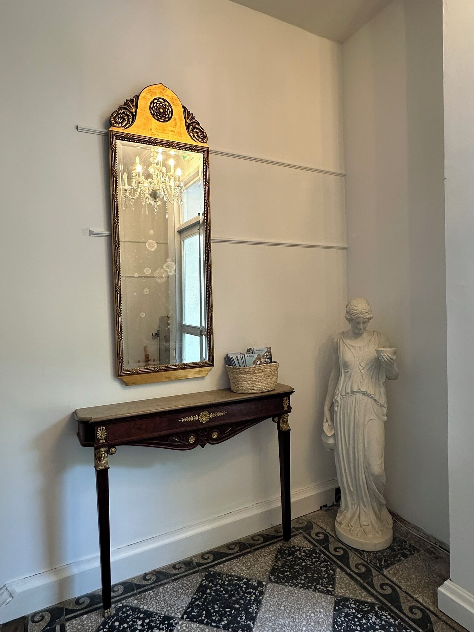 A hallway with a mirror, a statue, and a console table with a basket.