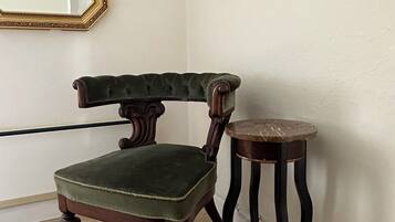 A corner room with a green upholstered chair, a small round table, and a mirror on the wall.