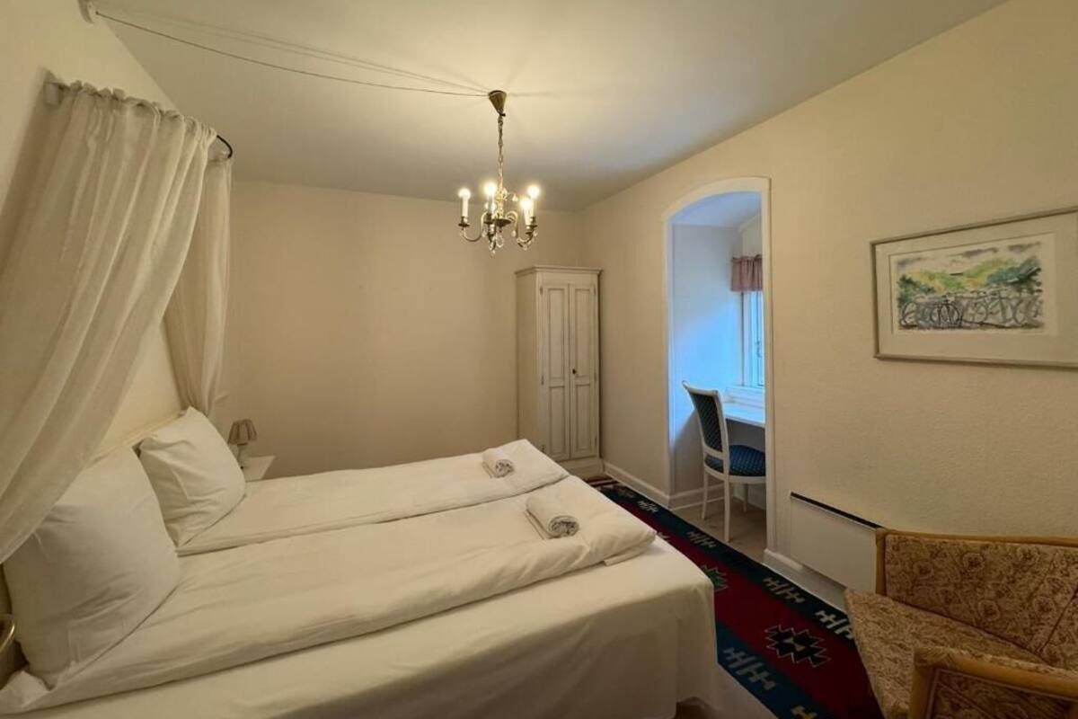 A hotel room with two beds, a chandelier, a chair, and a painting on the wall.