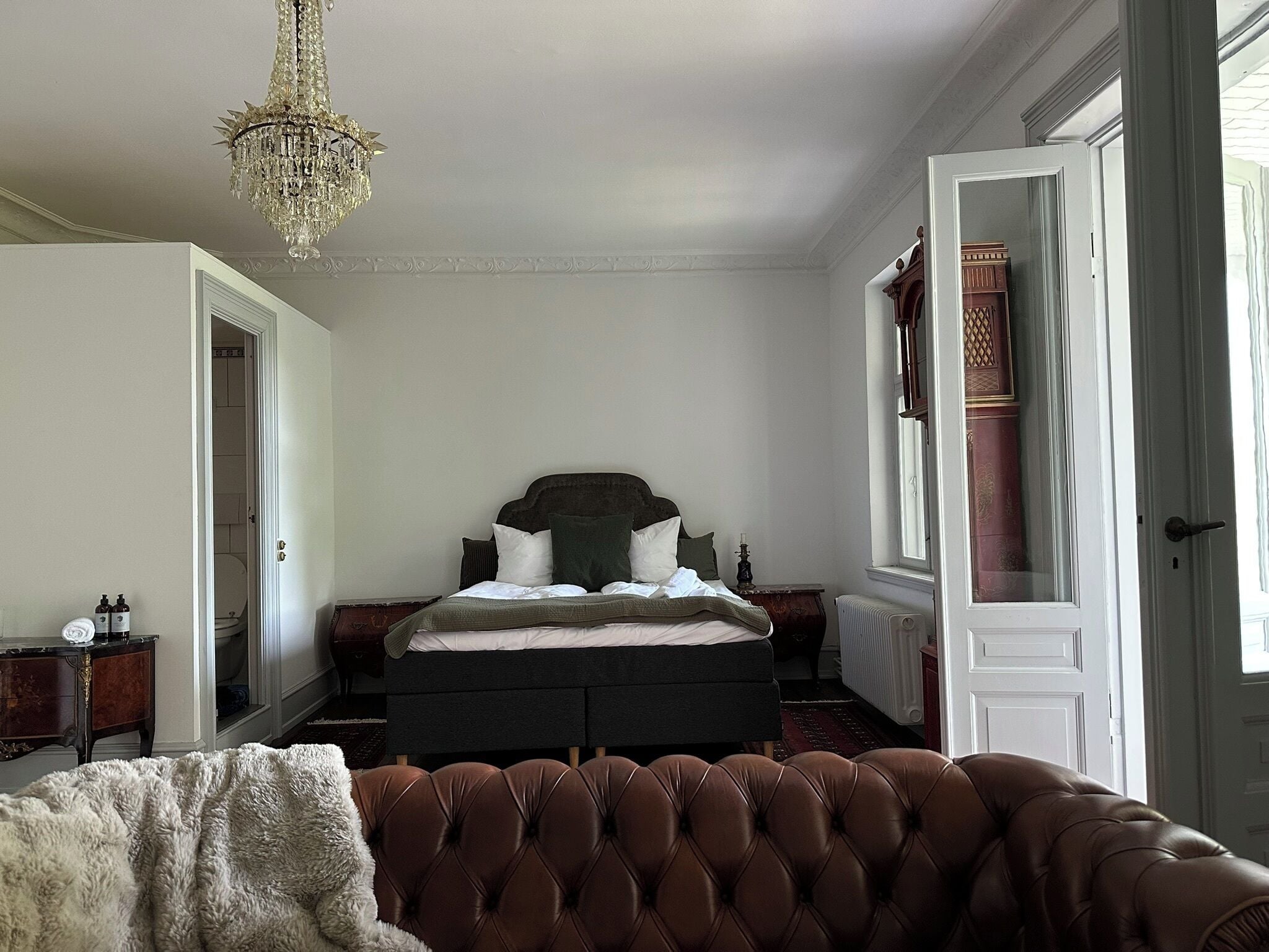 Un dormitorio con cama, candelabro, ventana y puerta.