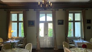 A dining room with tables set for service, a chandelier, and large windows with curtains. - Liselund Ny Slot (Borre)
