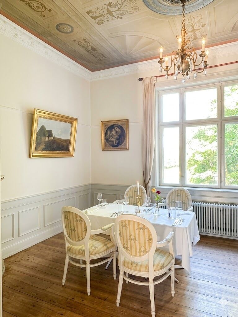 Comedor con una mesa preparada para cuatro, techo ornamentado y dos cuadros en la pared.