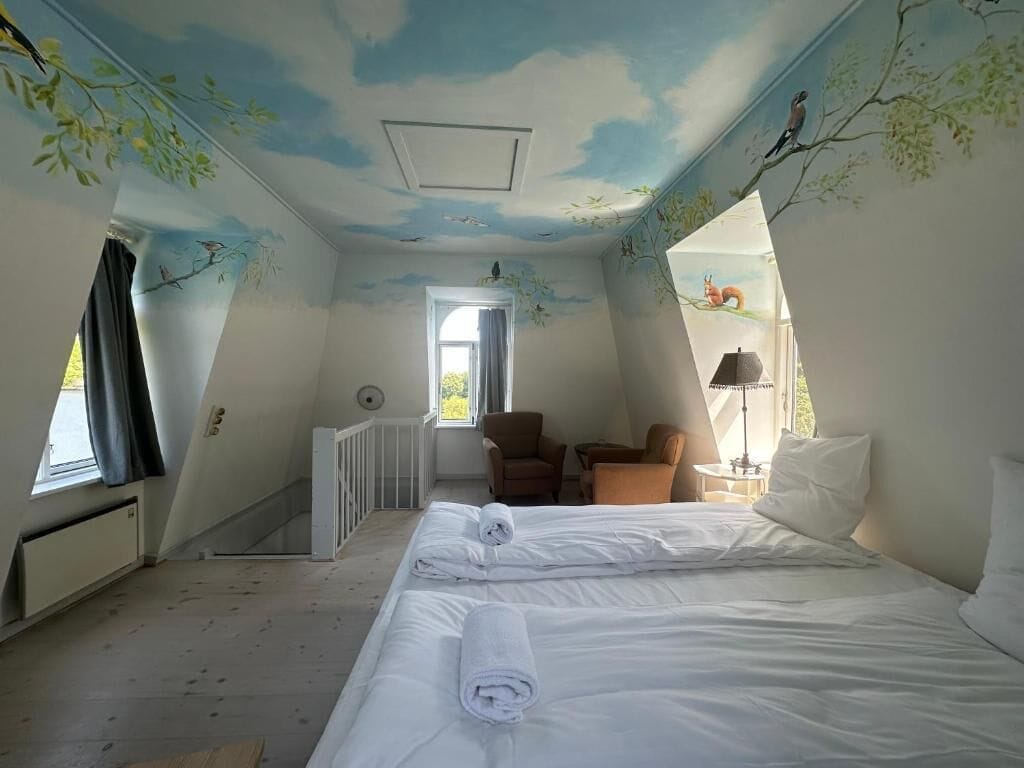 A room with a bed, two chairs, a table, and a window.