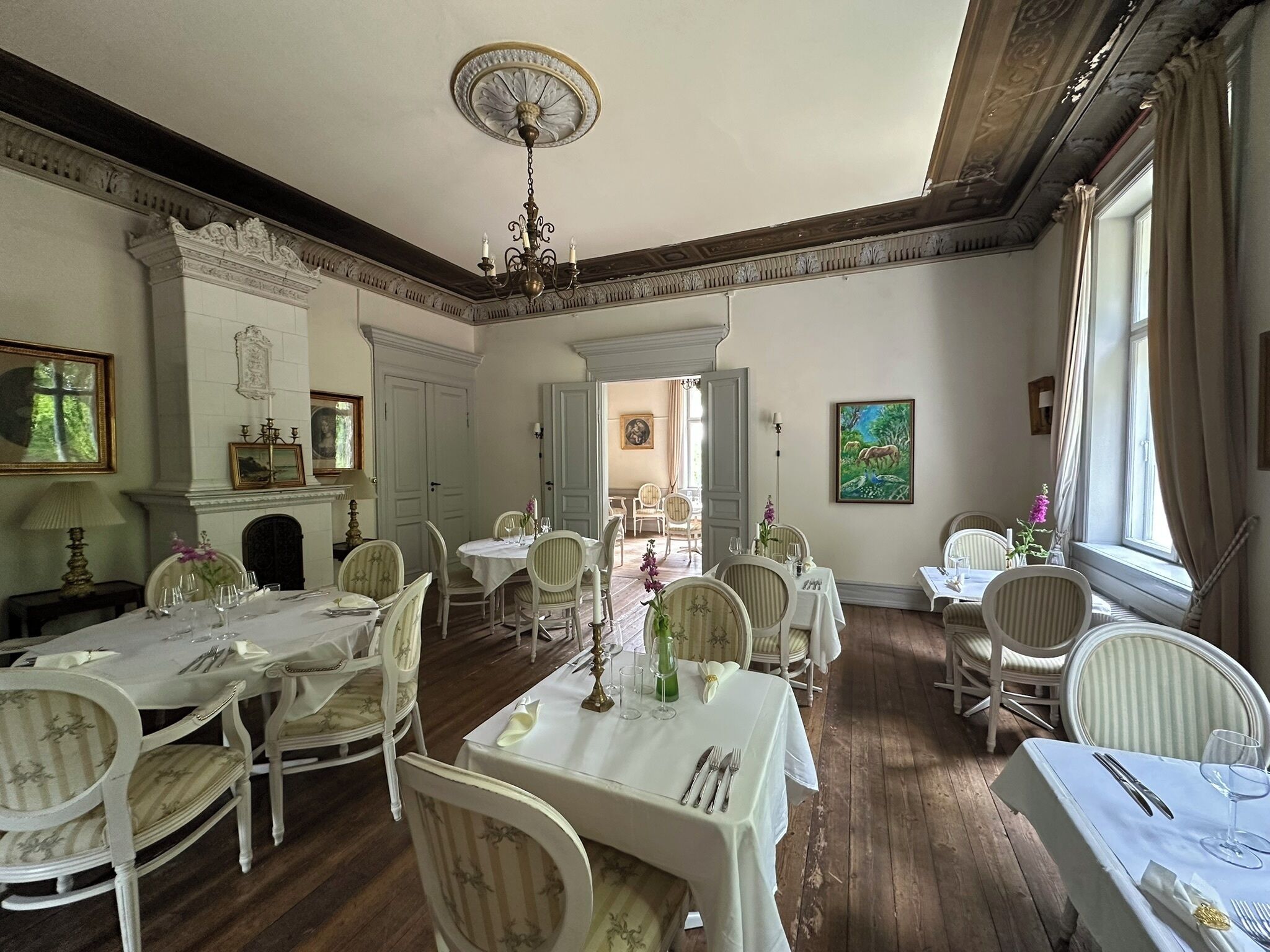 A dining room with white tables and chairs, a chandelier, and a fireplace.