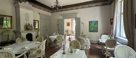 A dining room with white tables and chairs, a chandelier, and a fireplace.