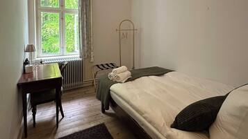 Un dormitorio con cama, escritorio, radiador y ventana con cortinas.