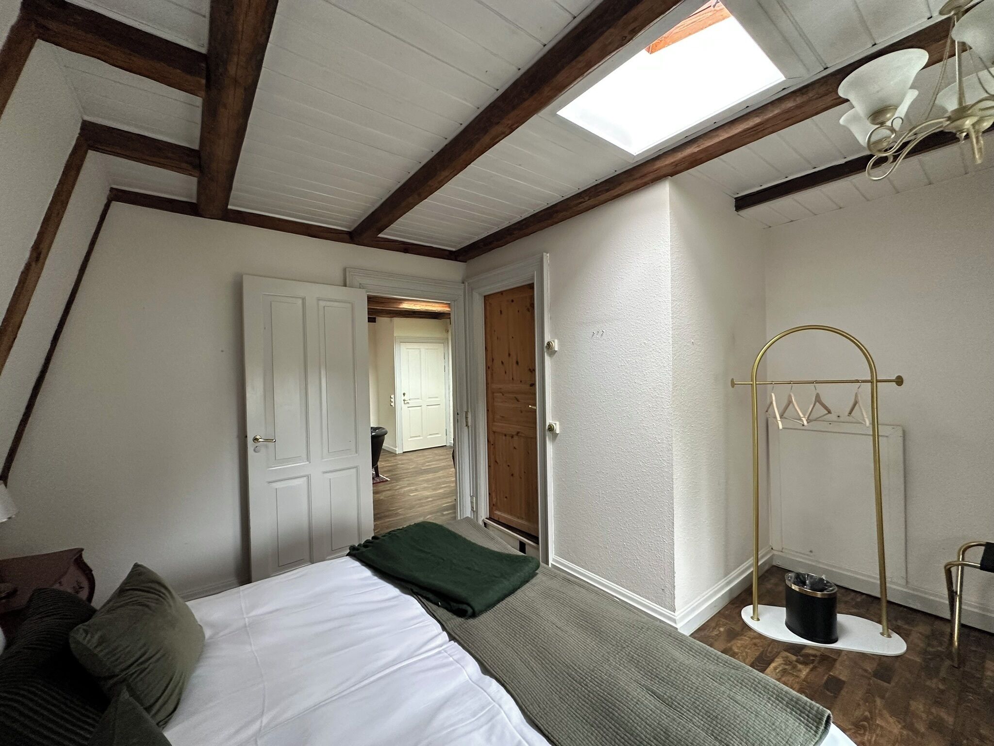 A bedroom with a bed, a bench, a hanging light fixture, and a door leading to another room.