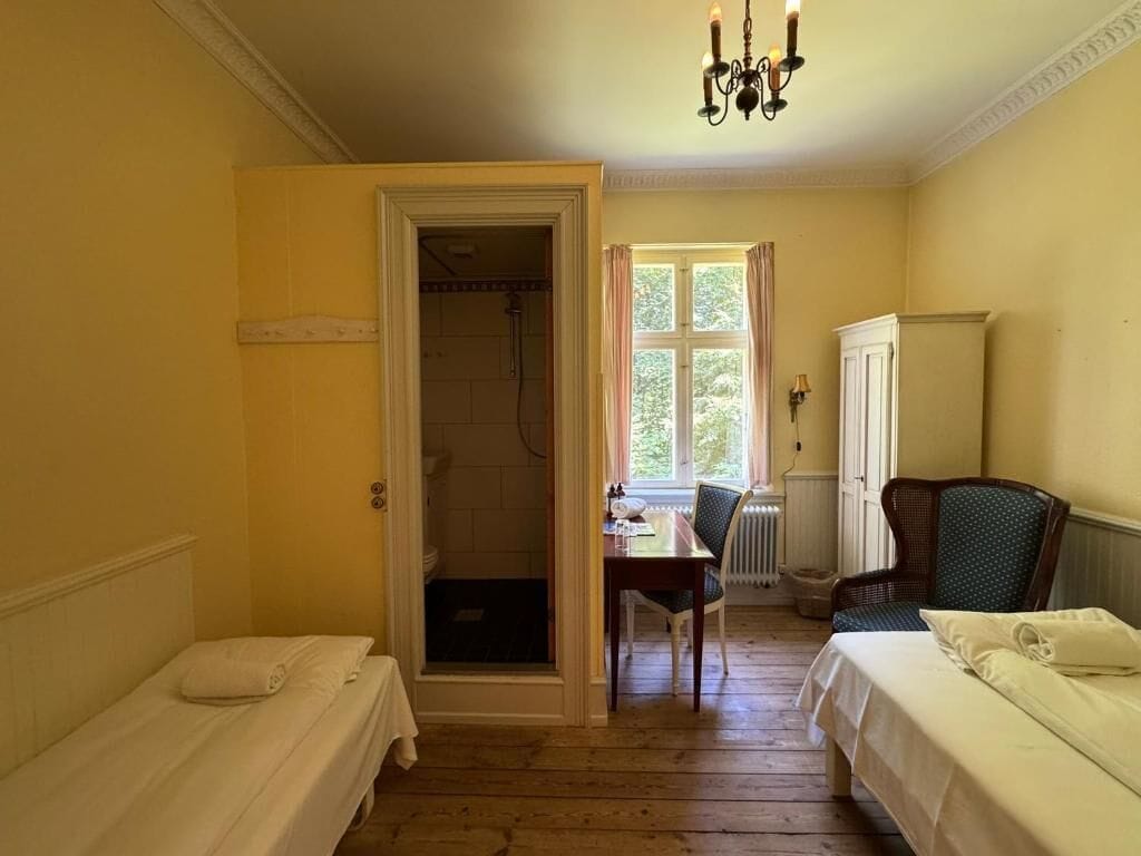 Una habitación con dos camas, una mesa, una silla, un radiador y una ventana con cortinas.
