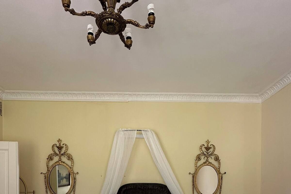 A bedroom with a four-poster bed, two bedside tables, a chandelier, and two ornate mirrors.