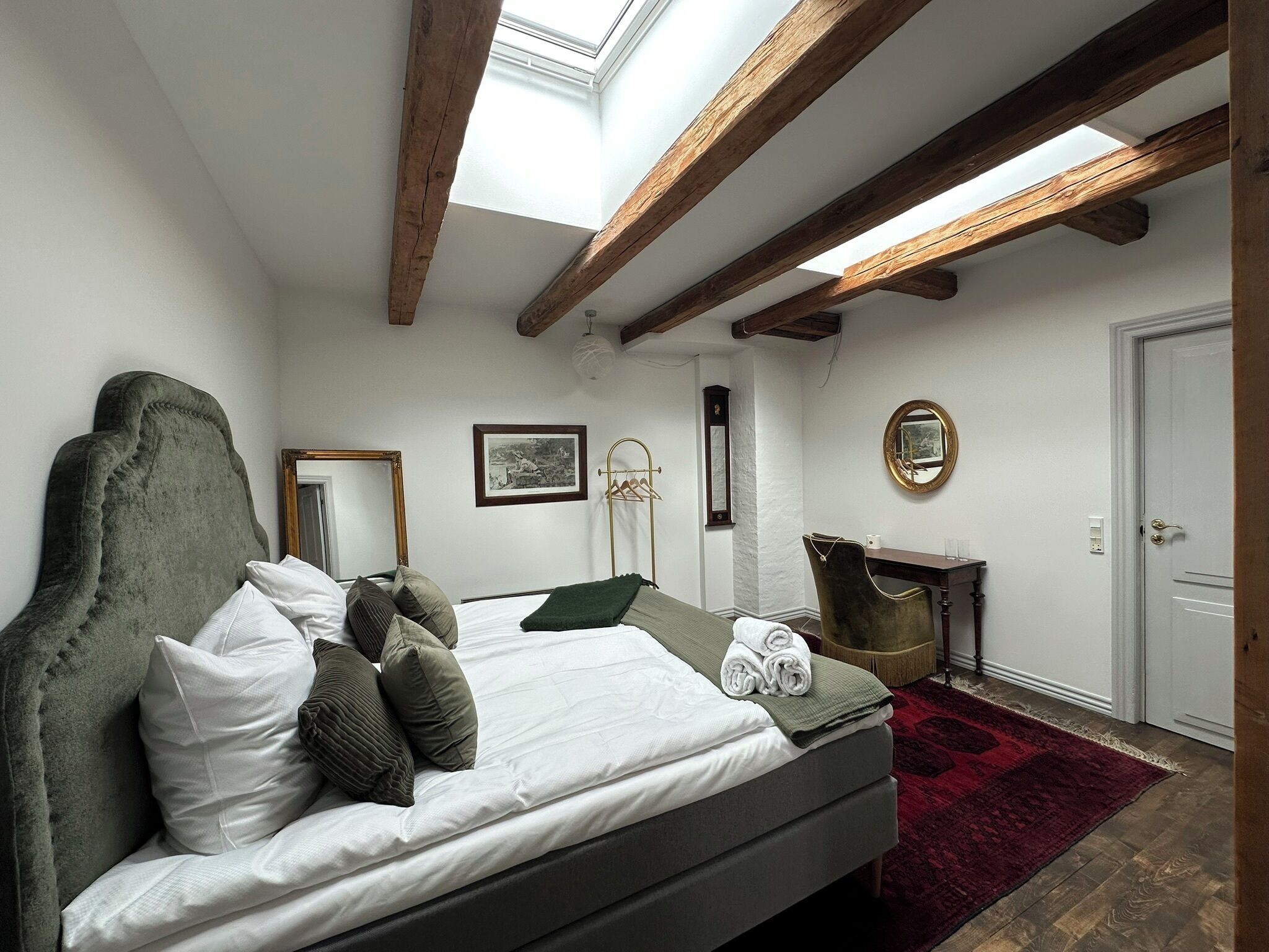 A bedroom with a bed, a mirror, a dresser, and a skylight.