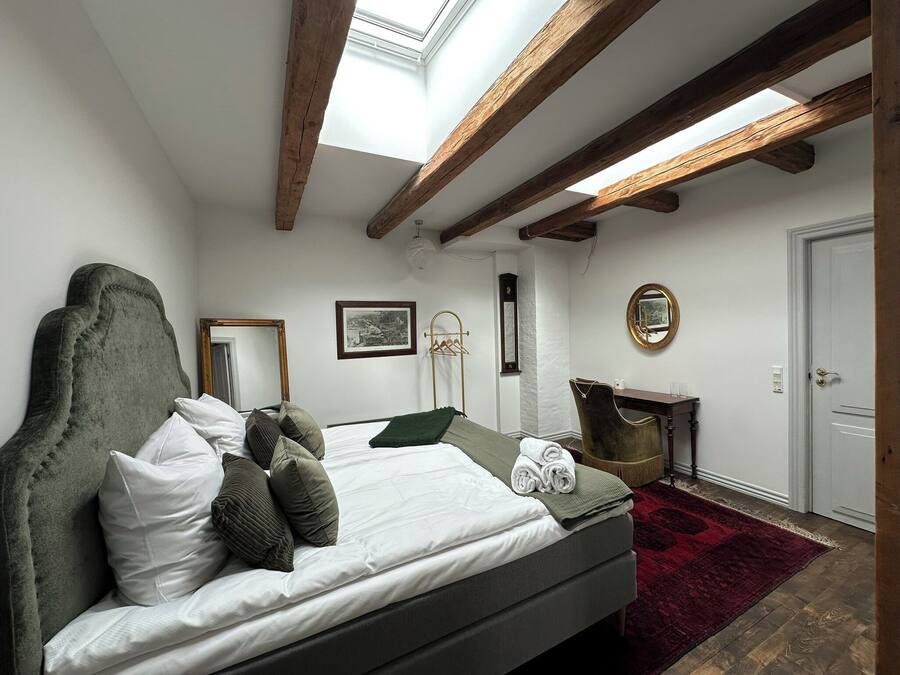A bedroom with a bed, a mirror, a dresser, and a skylight.