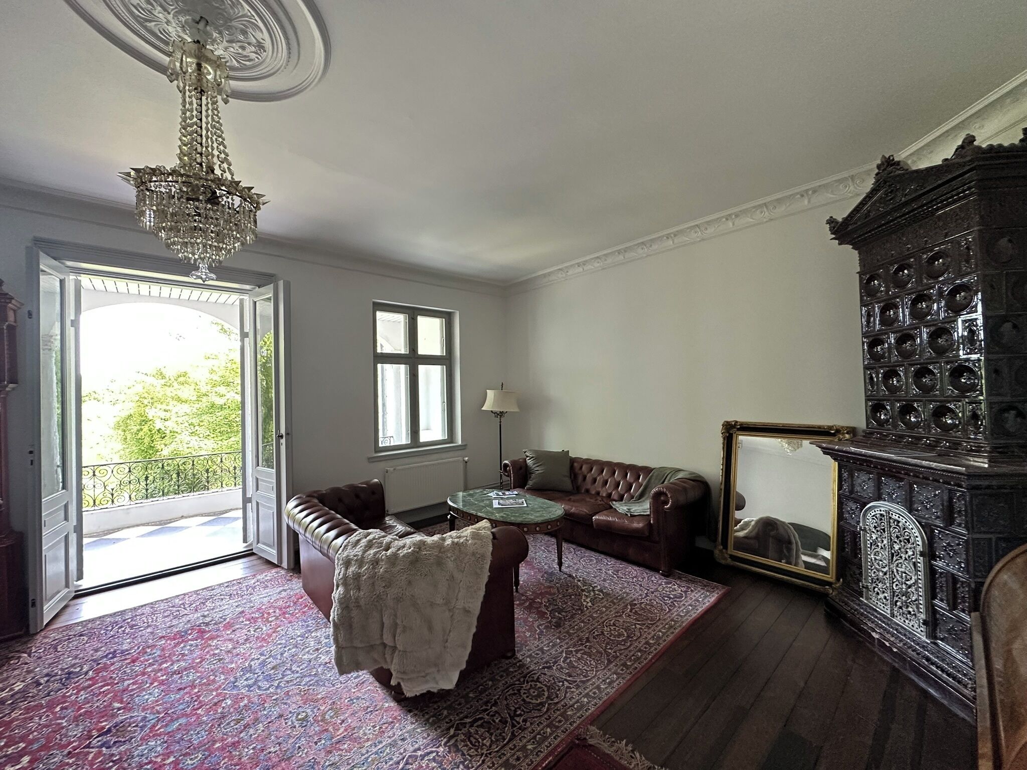 Una habitación con un sofá de cuero marrón, un tapete estampado, una araña y un mueble de gran tamaño y decorado.