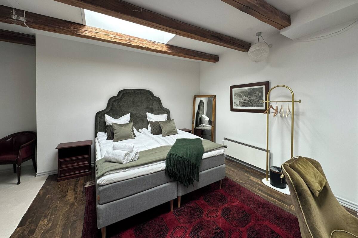 A bedroom with a bed, a chair, a bedside table, a mirror, a coat rack, and a window.