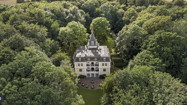 A large, historic building surrounded by dense forest, with a central courtyard and multiple windows. - Liselund Ny Slot (Borre)