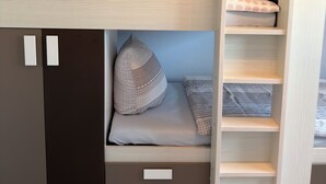 Una cama litera con un espacio de almacenamiento debajo, un pequeño estante y un armario.