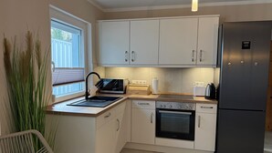 Una cocina moderna con armarios blancos, un refrigerador negro, horno empotrado, microondas y un lavamanos con grifo.