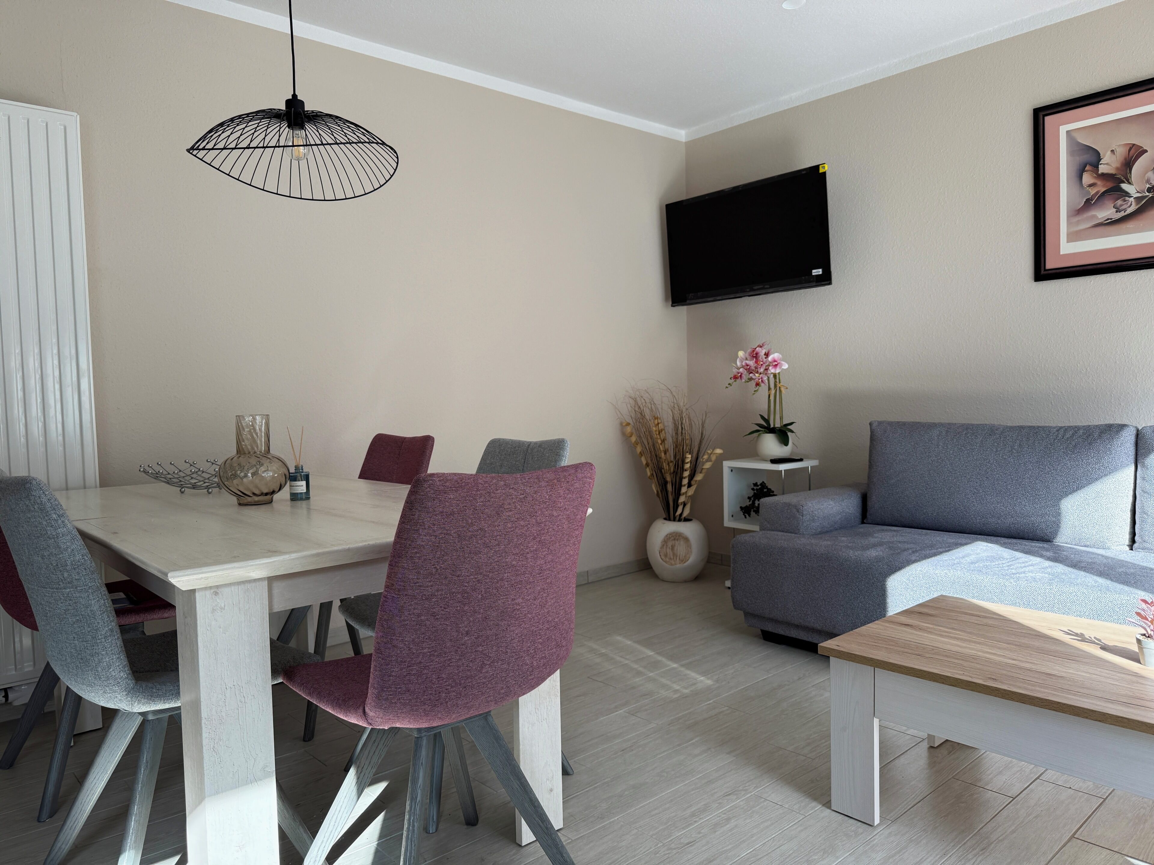 Un salón moderno con comedor, sofá gris y televisor montado en la pared.