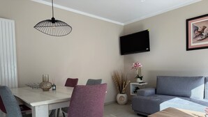 Un salón moderno con comedor, sofá gris y televisor montado en la pared.