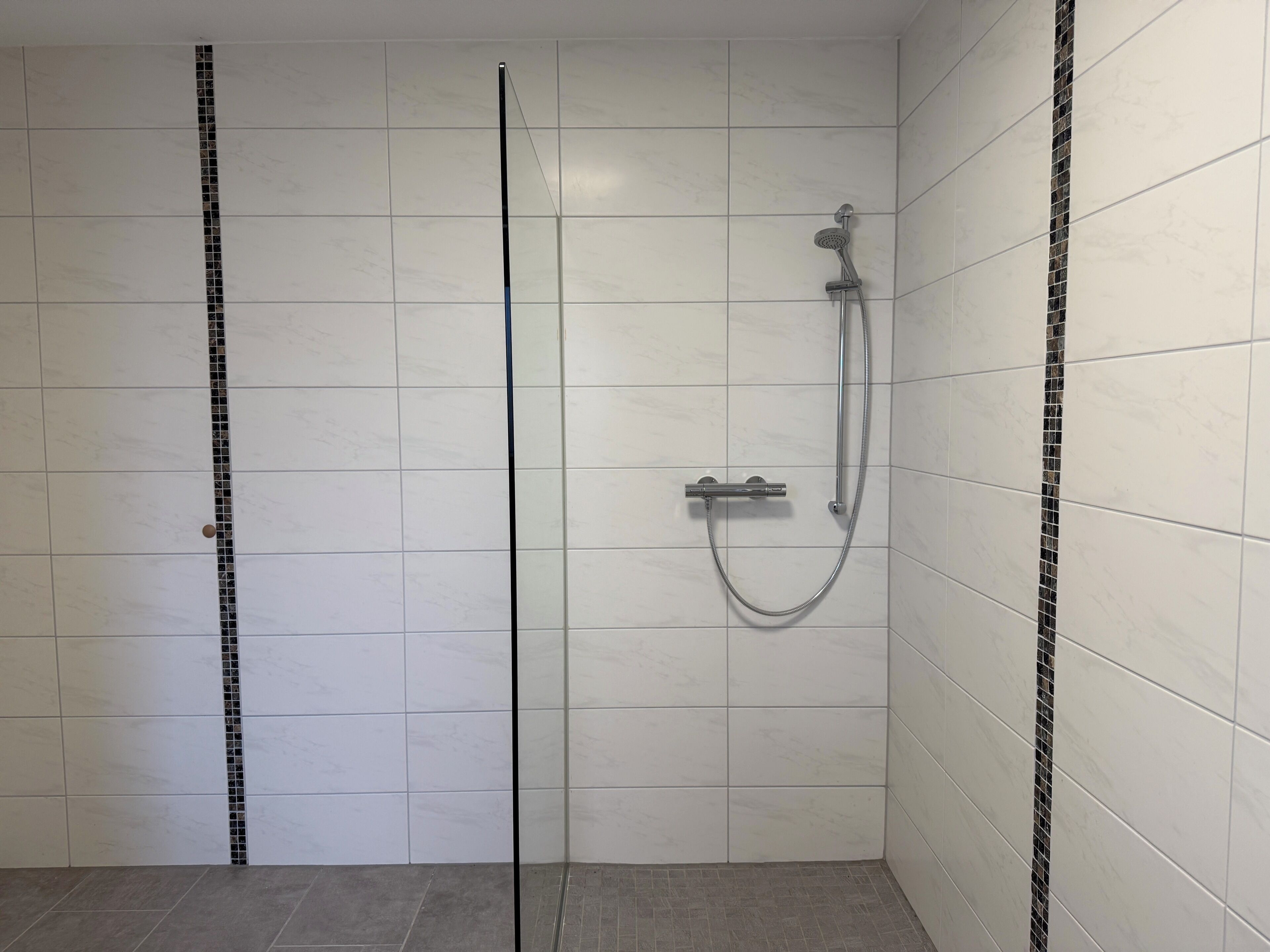 Un espace douche doté d’une porte en verre, de murs carrelés et d’un pommeau de douche.