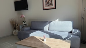 Una sala de estar moderna con un sofá gris, una mesa de centro de madera, un televisor de pantalla plana, un cuadro enmarcado y una lámpara de pie.