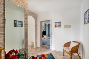 Una habitación con piso de madera, una silla de mimbre, un tapete colorido y una puerta que da a otra habitación.