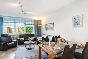 Una sala de estar moderna con comedor, sofás de cuero, una mesa de centro y vistas al exterior con vegetación.