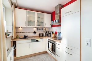 Una cocina compacta con armarios blancos, horno empotrado y cafetera.