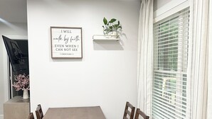 A dining area with a wooden table and chairs, a framed inspirational quote, a small plant on a shelf, and a window with blinds. - 3 bedroom House in Campobello fits 8 people  (Campobello)