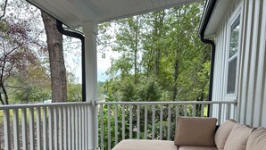 A covered porch with a white railing, a wicker sofa with beige cushions, and a glass-top coffee table with a small plant. - 3 bedroom House in Campobello fits 8 people  (Campobello)