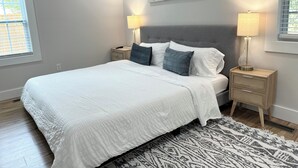 Een slaapkamer met een bed, twee nachtkastjes, een wanddecoratie in abstractie en een raam met zonwering.
