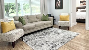 A living room with a sofa, armchair, and ottoman, a patterned rug, and a painting on the wall. - 3 bedroom House in Campobello fits 8 people  (Campobello)