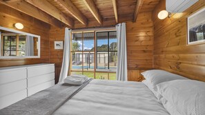 A wooden cabin bedroom with a bed, a dresser, and a view of a swimming pool. - Leumeah Peaceful rural views (Allambee Reserve)