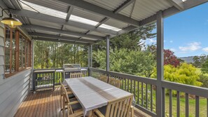 A covered outdoor deck with a table and chairs, a grill, and a view of a garden and hills. - Leumeah Peaceful rural views (Allambee Reserve)