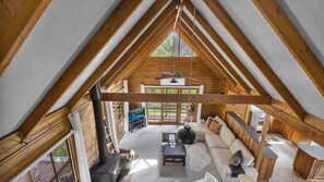A high-ceilinged wooden interior with a central seating area, large windows, and a visible outdoor deck.
